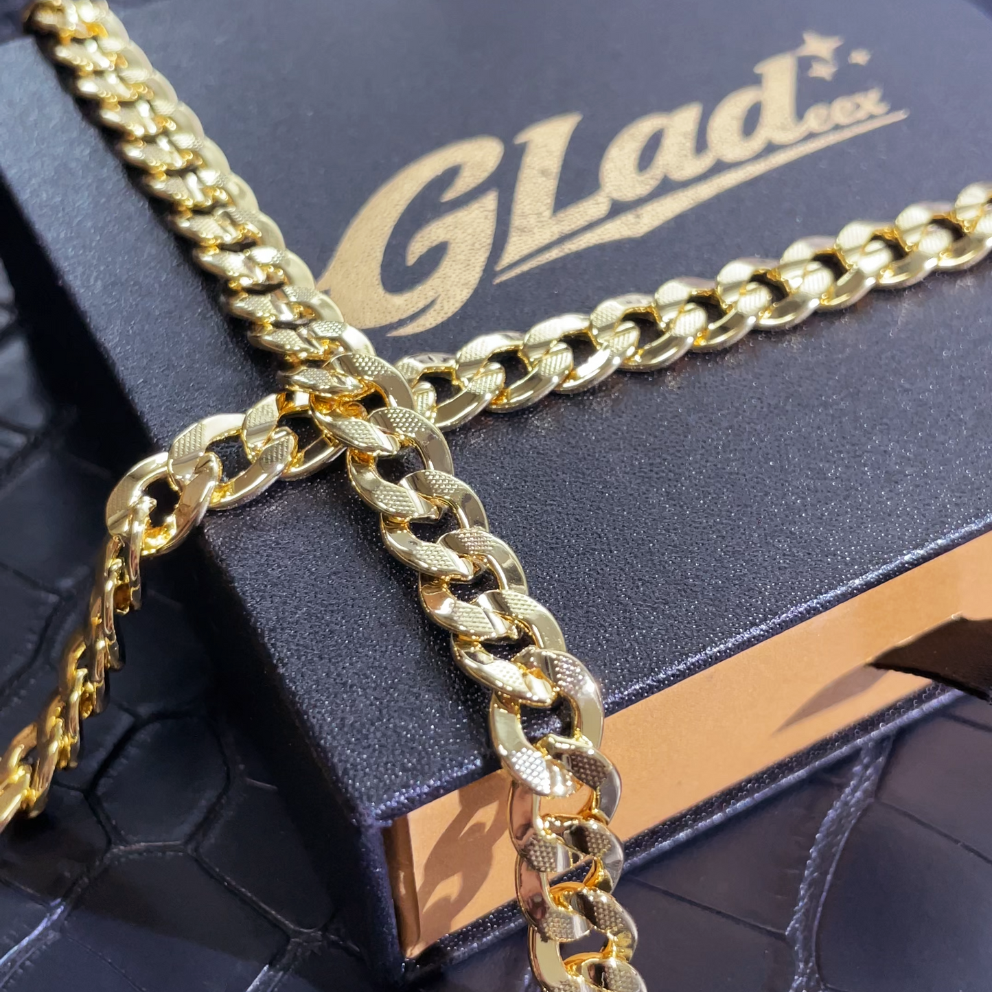Close-up of an 8mm 14K gold plated carved Cuban link chain over a GLADEEX box