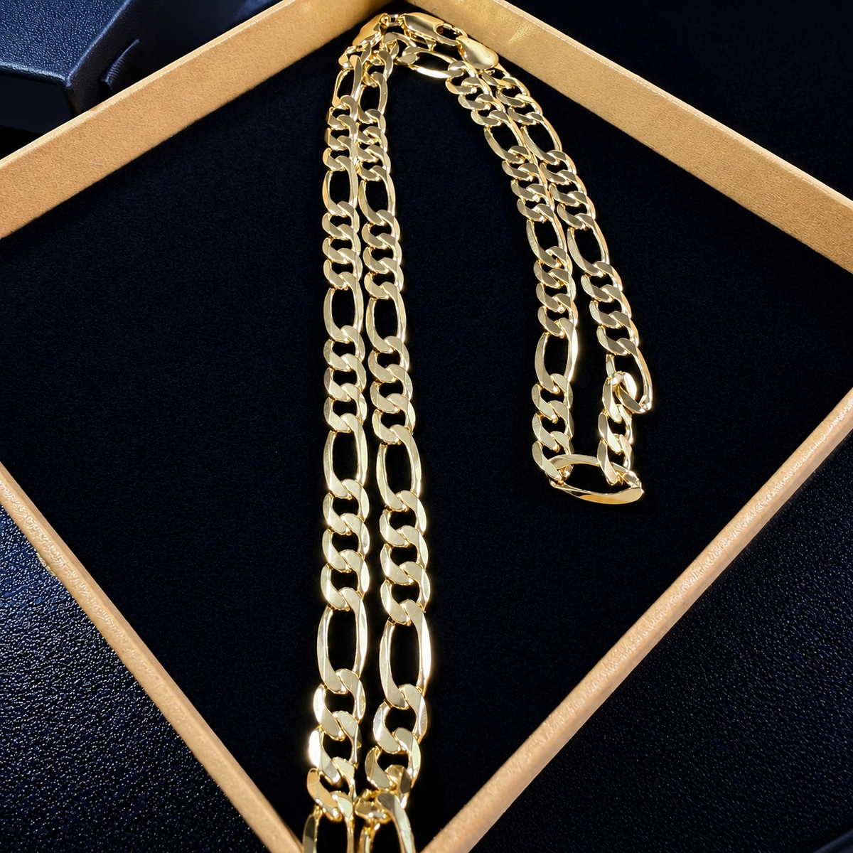 14K gold plated Figaro chain arranged inside a black and gold display box
